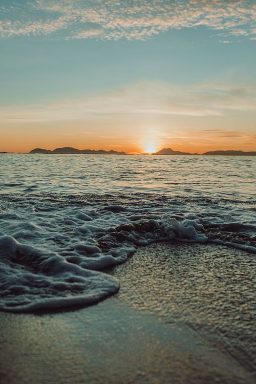Free A tranquil ocean scene at sunset with gentle waves lapping the shore and a bright sky. Stock Photo