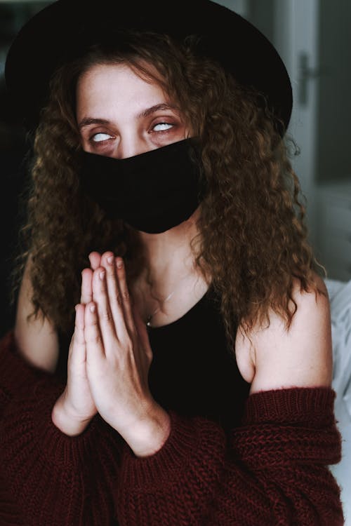 Enigmatic woman in mask praying with hands clasped