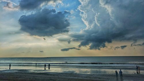 Free A stunning coastal scene with a dramatic cloudy sky and people walking along the beach. Stock Photo