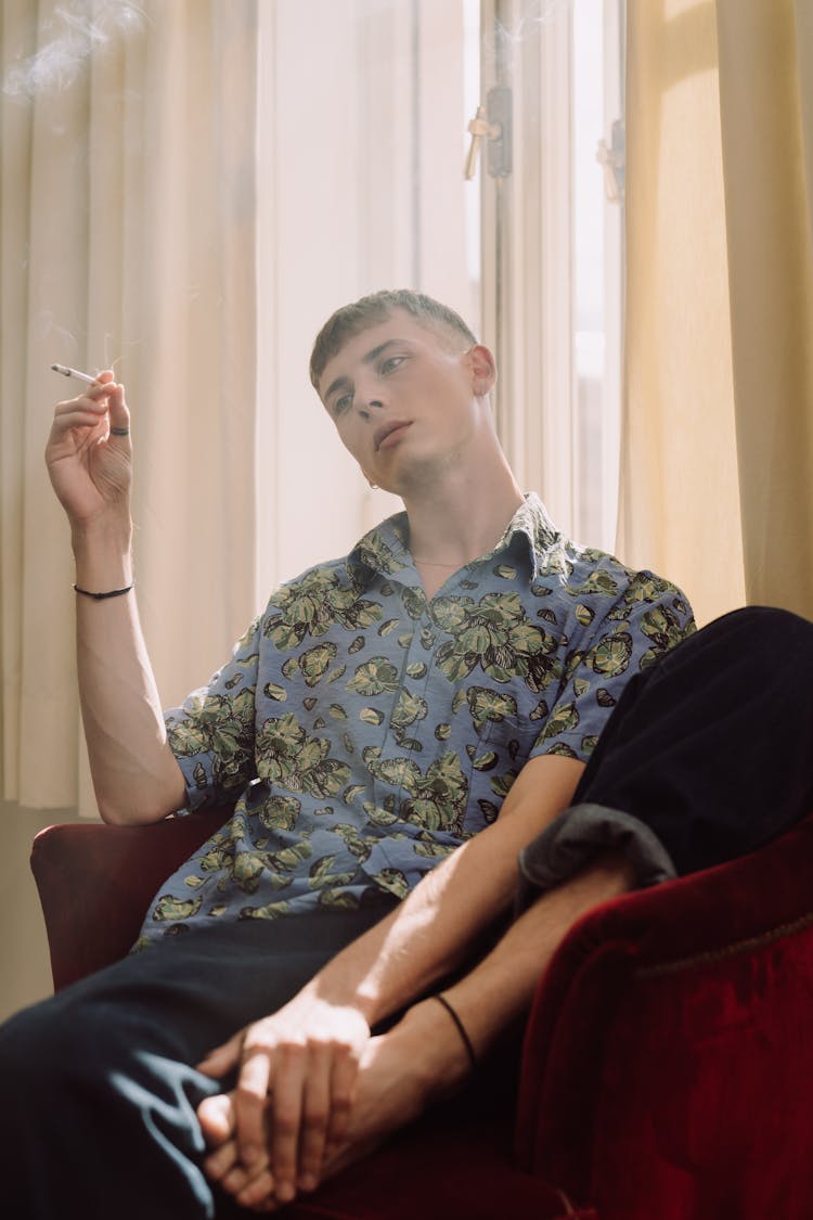 A Man Sitting On A Couch Holding His Foot While Smoking