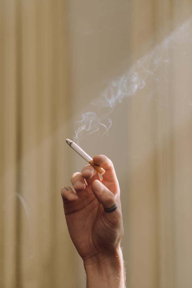 A Tattooed Thumb Hand Holding A Lighted Cigarette