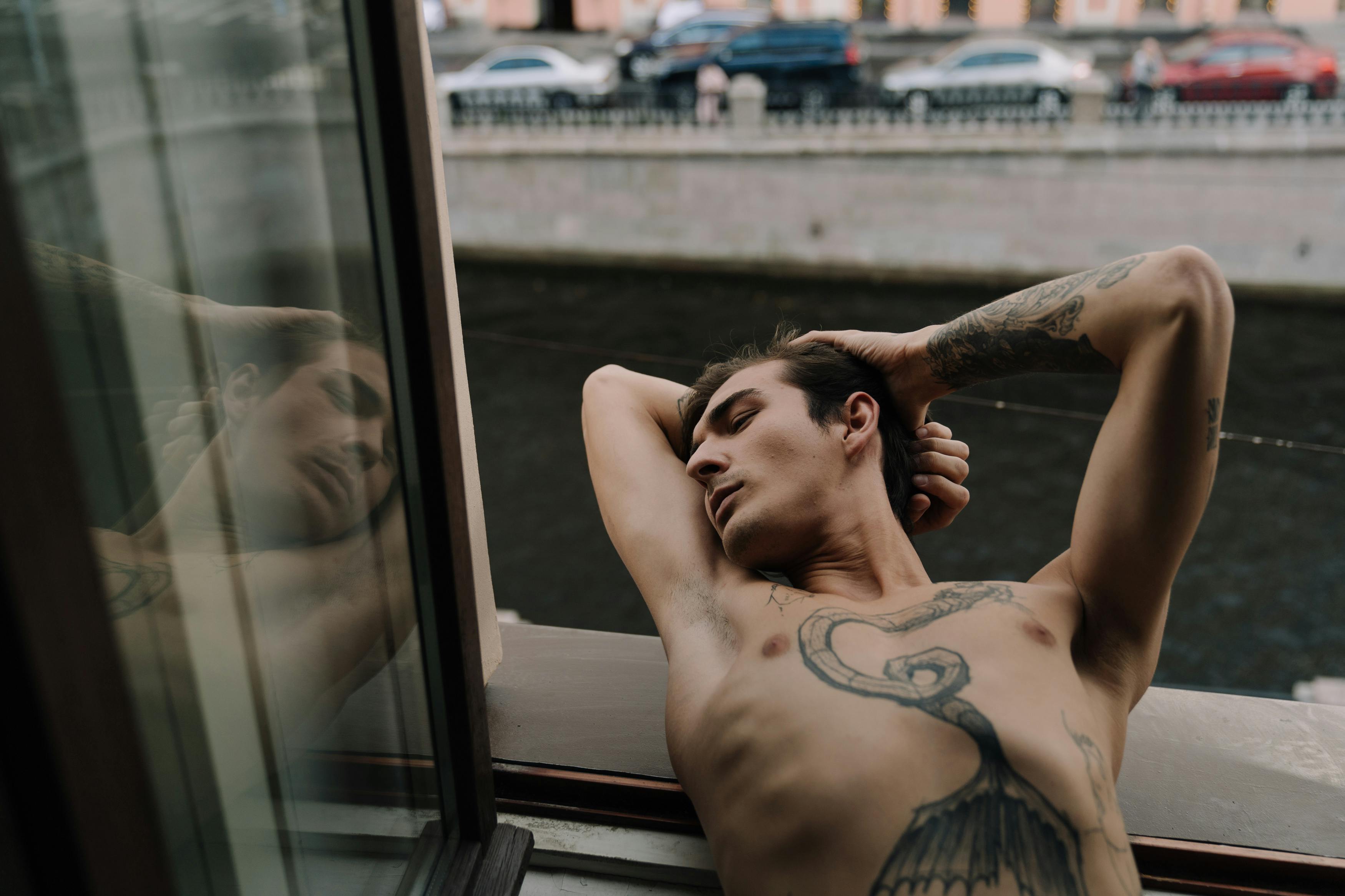 Topless Man with Tattoo Lying on Window Sill · Free Stock Photo