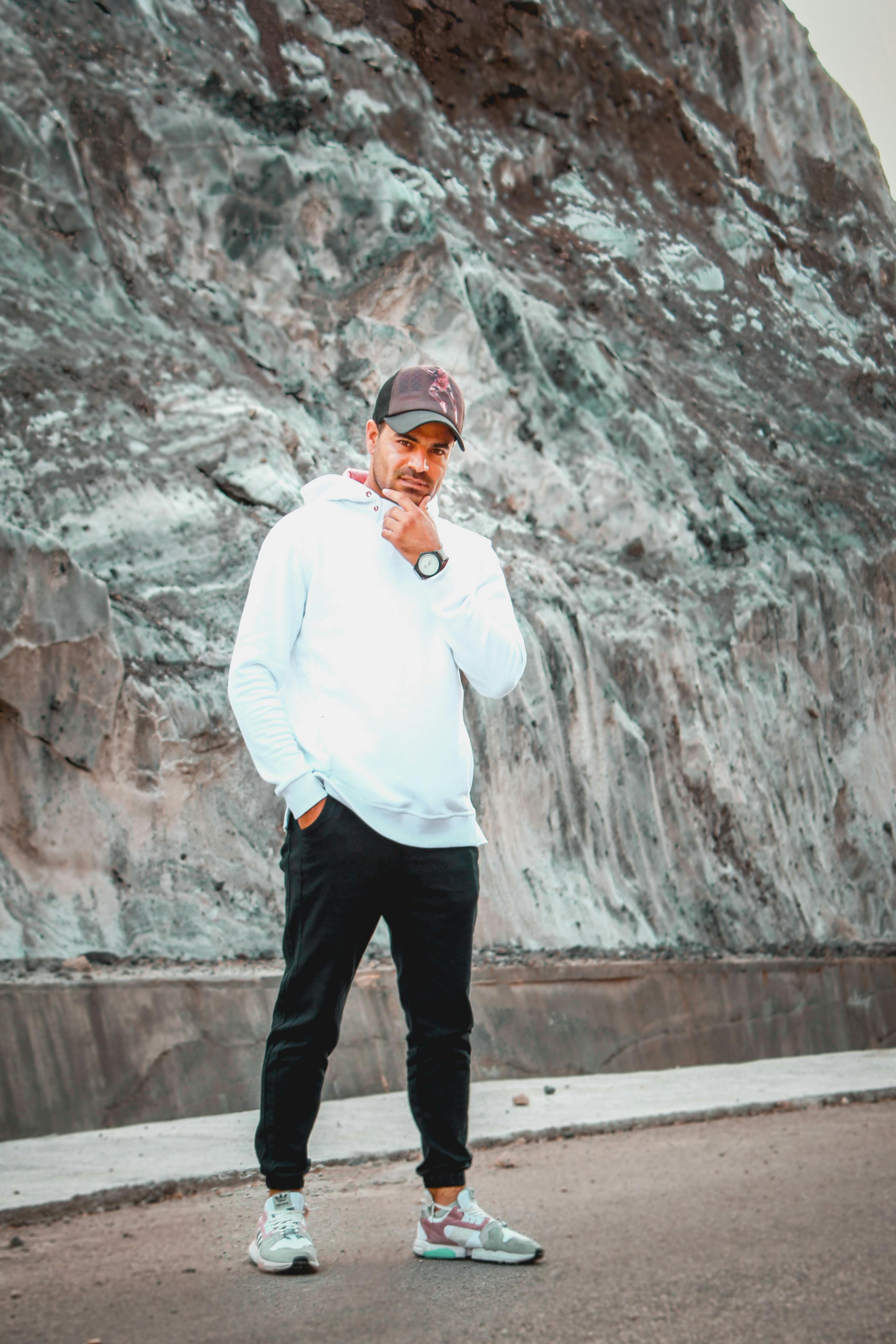 man in white long sleeve shirt and black pants standing with hand on chin