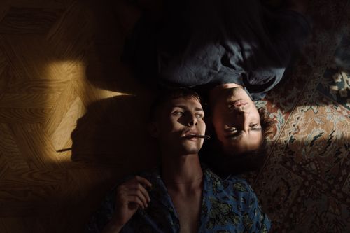 Free A moody portrait of two young adults lying together on a sunlit floor, conveying emotion and connection. Stock Photo