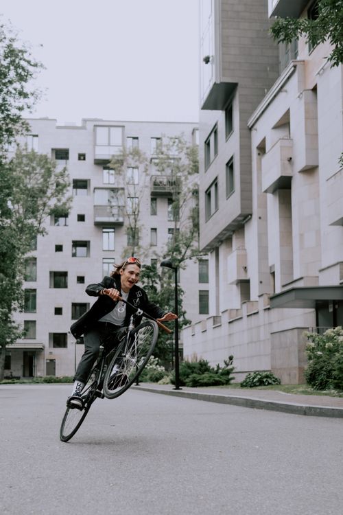Free Young man performs a bicycle stunt in an urban environment with high-rise buildings. Stock Photo