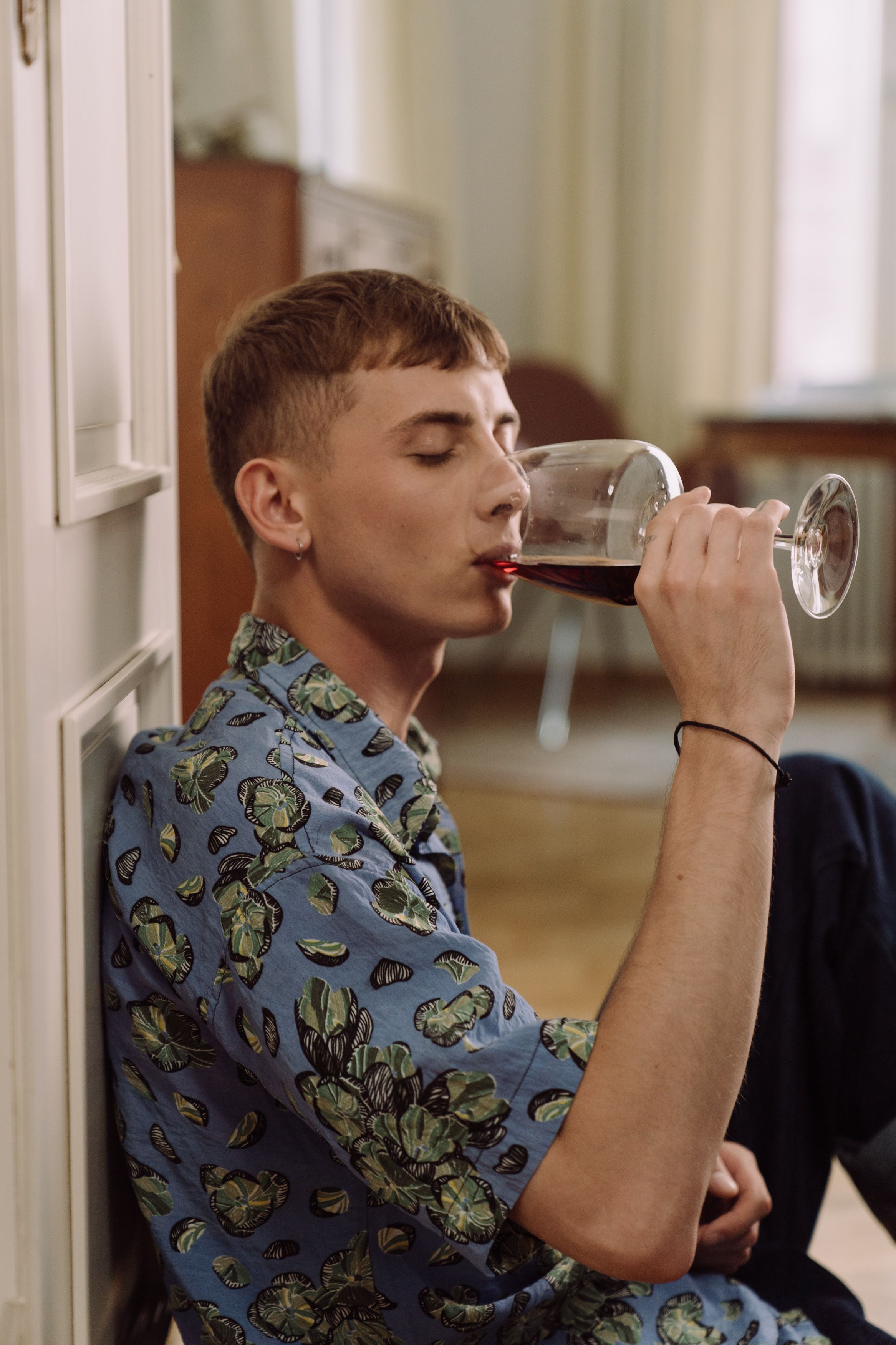 A young adult sipping red wine while sitting indoors, capturing a relaxed moment.