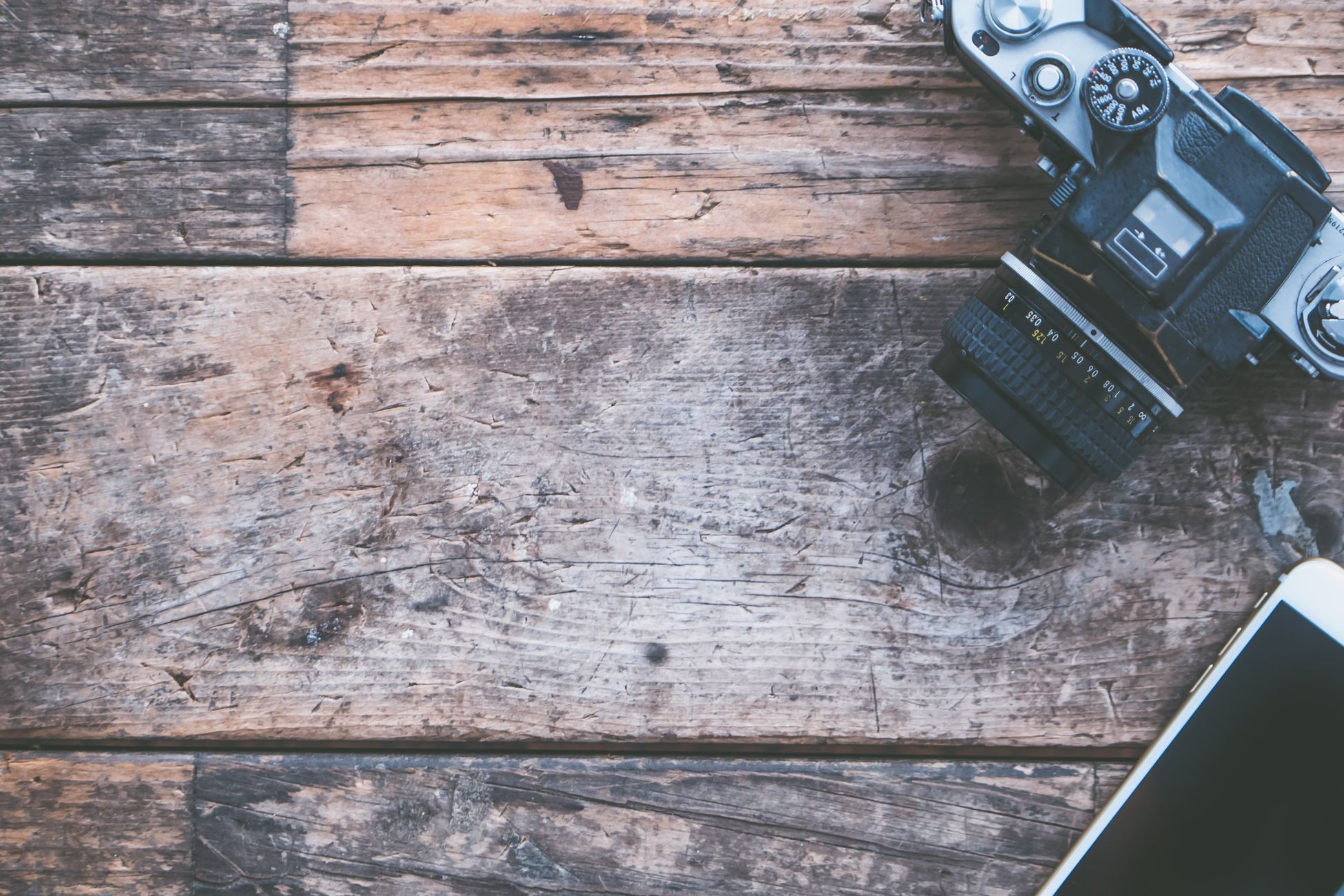 Flat lay of vintage camera and smartphone on rustic wooden planks, perfect for creative projects.