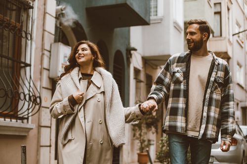 Free Happy couple holding hands while walking together down a picturesque city street. Stock Photo