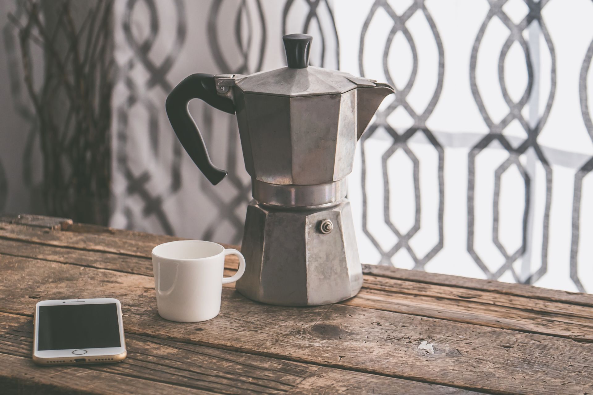 Moka pot and coffee cup on wooden table with smartphone, perfect for cozy mornings.