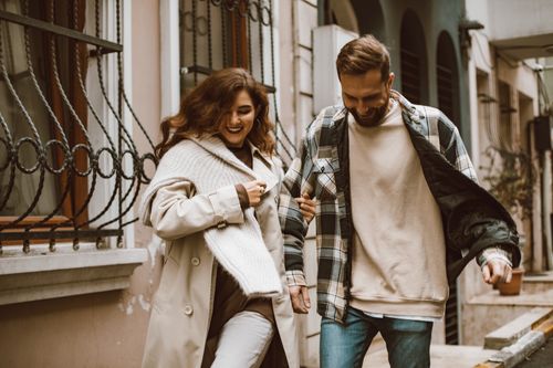 Free Joyful couple walking arm in arm down an urban street, smiling and enjoying their day. Stock Photo