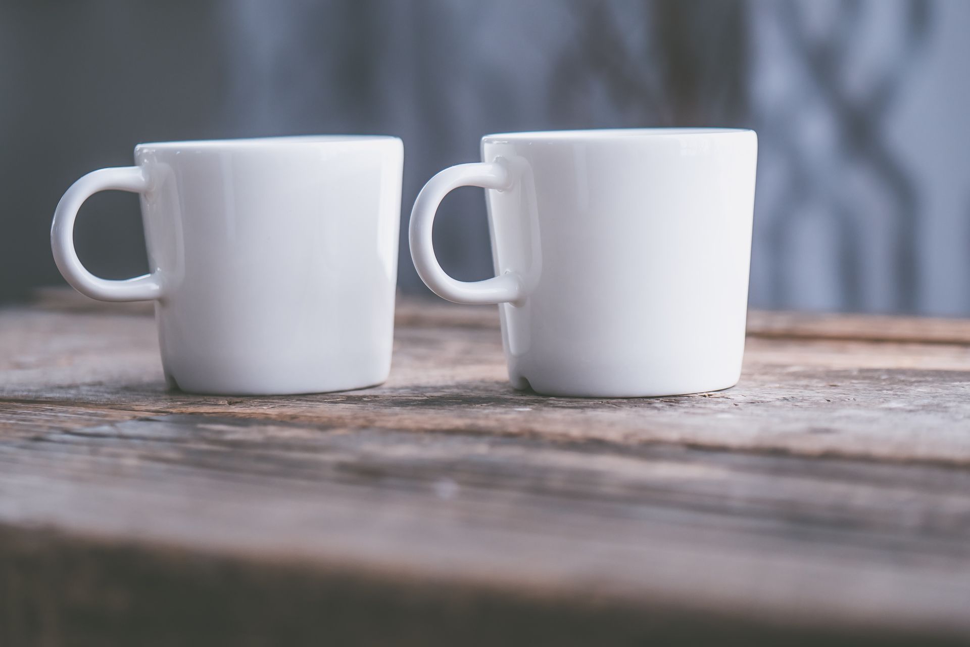 Close-up of two white ceramic cups on a rustic wooden table, featuring soft natural light.