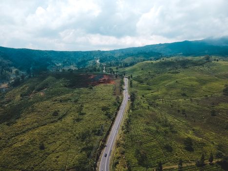 Aerial shot of a scenic countryside road cutting through lush green hills under cloudy skies.