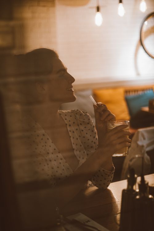 Free Woman enjoying a drink in a warmly lit restaurant with ambient lighting. Stock Photo