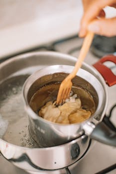 A close-up view of dumplings being cooked in a pot of boiling water, stirred by a wooden fork.