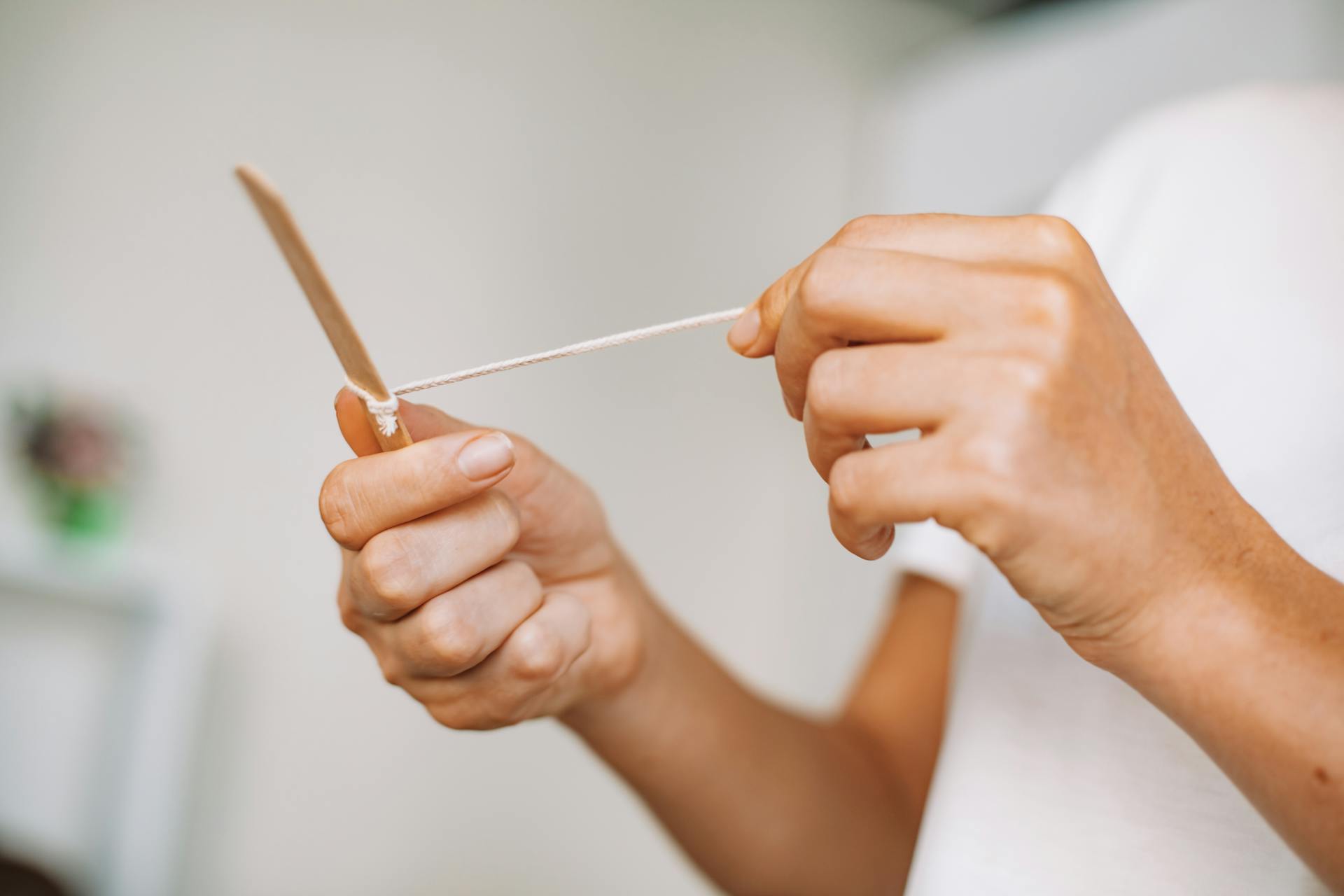 Hands holding a craft stick with string, displaying a creative DIY activity.