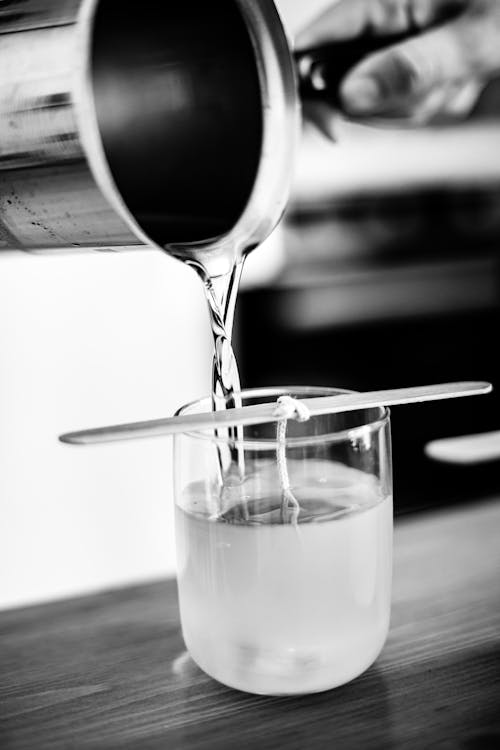 Person Pouring Liquid Wax into a Glass with a Wick on a Stick 