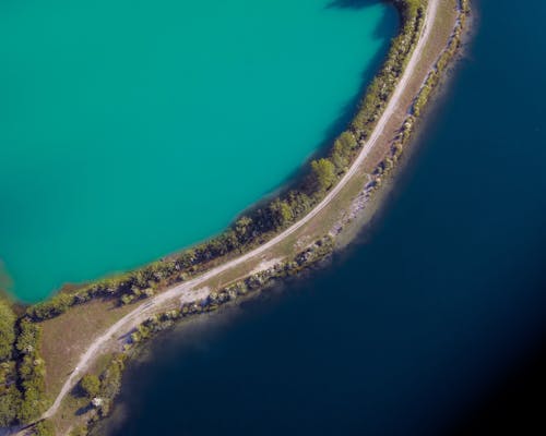 Aerial view of narrow curvy road running between lagoon of rich turquoise color and ocean surface with dark blue water