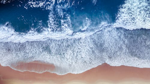 Top view of foamy surf of stormy sea in rich ultramarine color rolling over wet coastline