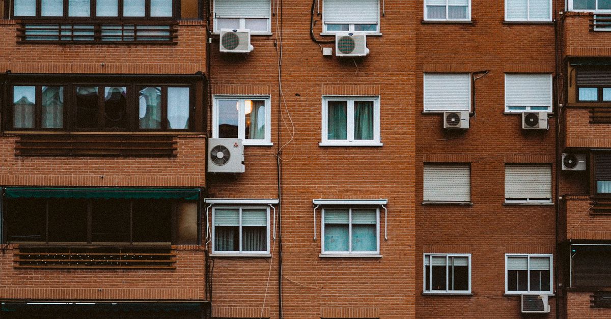A detailed view of an orange brick apartment facade with windows and air conditioners.