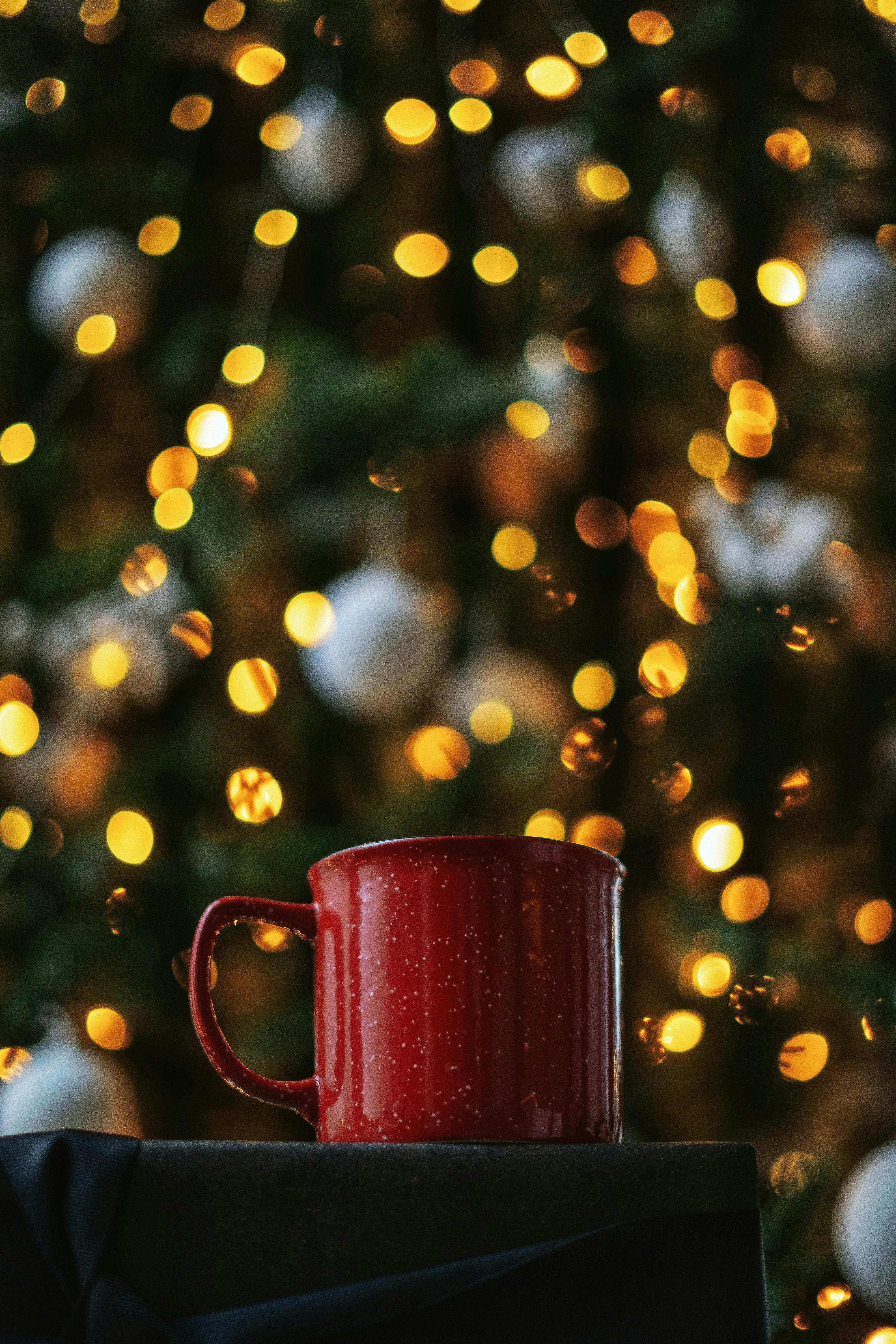 Red mug with bokeh Christmas lights in the background, evoking holiday warmth and coziness.