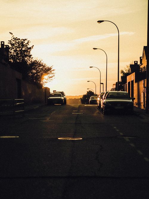 Free Tranquil urban street scene at sunset with parked cars and warm tones. Stock Photo