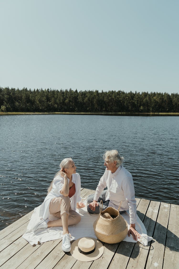 A Elderly Couple Having A Picnic In Wooden Platform By The Lake