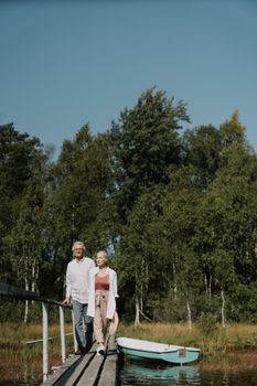 一对老年夫妇在碧绿湖边郁郁葱葱的木码头上平静地散步