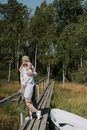 Woman in White Dress Shirt and Black Pants Standing on Brown Wooden Bridge