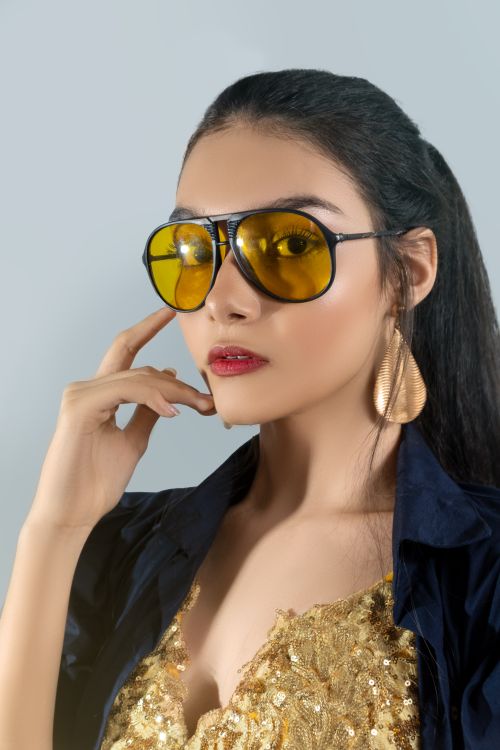 Free A fashionable young woman wearing yellow sunglasses and striking a pose in a studio setting. Stock Photo