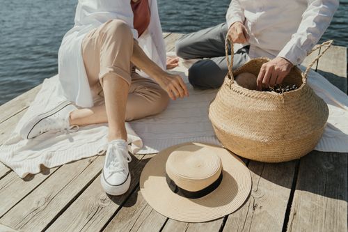 Free Couple enjoying a lakeside picnic with a woven basket on a relaxing sunny day. Stock Photo