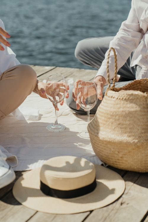 Free Couple enjoying a romantic picnic with wineglasses on a pier by the water. Stock Photo