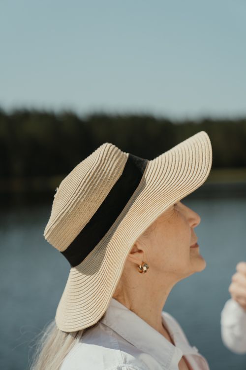 Free Elderly woman in a straw hat enjoying a sunny day by the water. Stock Photo