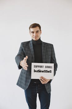 Photo by Gustavo Fring A man in corporate attire holds a sign supporting small businesses, studio setting.