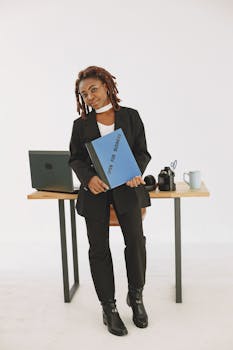 Portrait of a confident businesswoman holding an 'Open for Business' binder in a modern office setting.