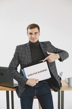 Professional man in jacket pointing to 'Open for Business' sign, indicating business readiness.