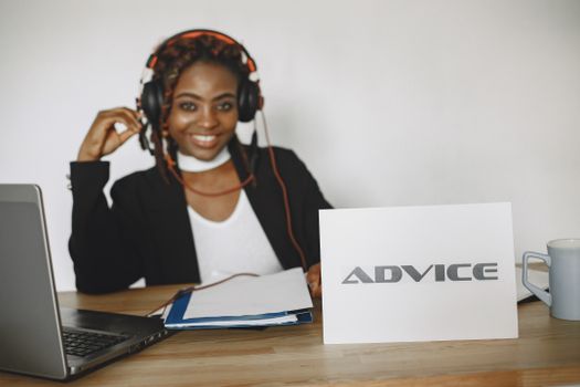 A cheerful woman in headphones providing online advice via laptop at her office desk.