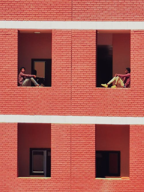 Two Men Sitting in the Windows of a Red Brick Building