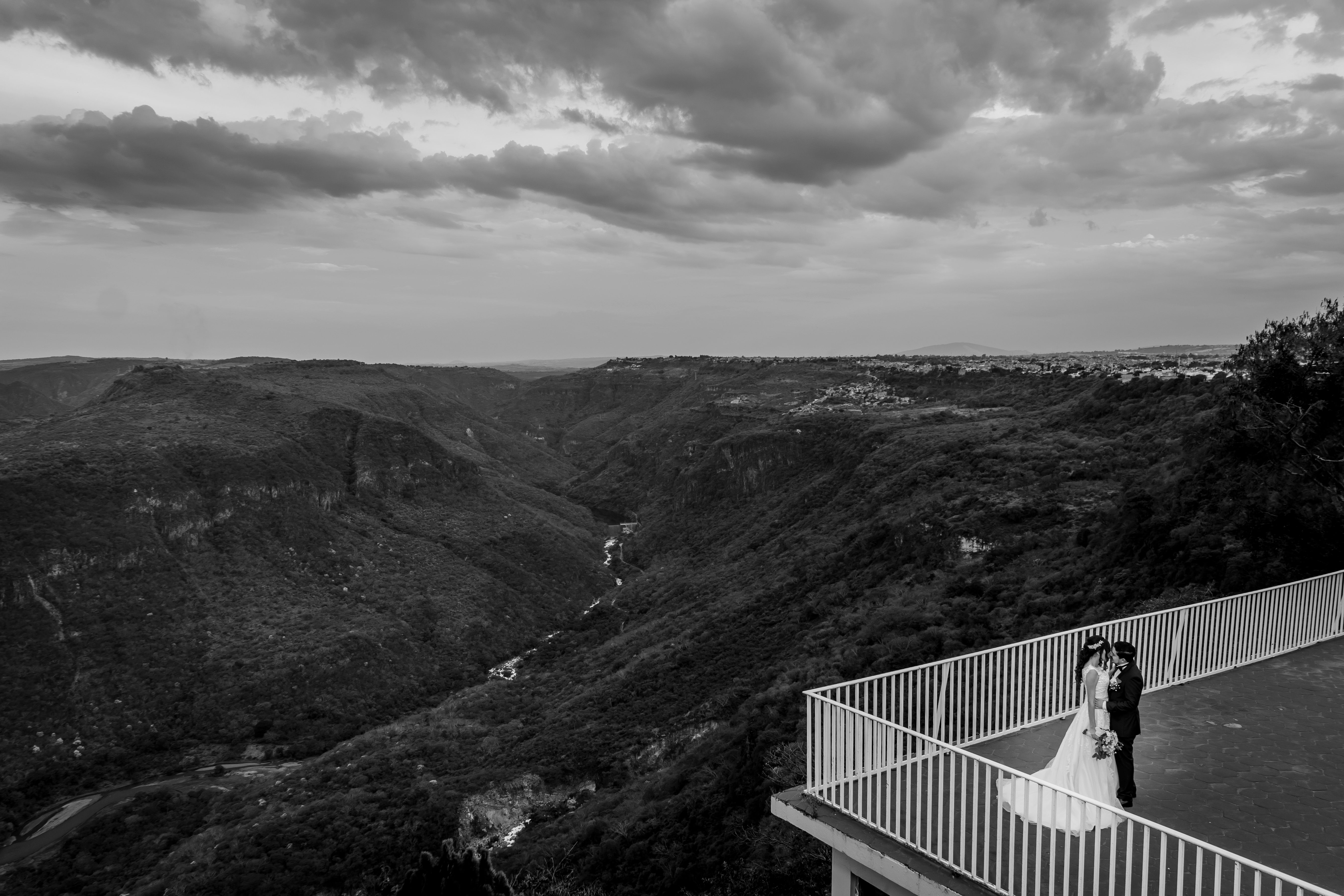 A romantic black and white image of a wedding couple on a balcony overlooking a vast scenic canyon.