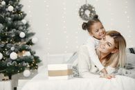 A mother and daughter enjoying a cozy moment by a Christmas tree with presents, symbolizing family love and festive joy.