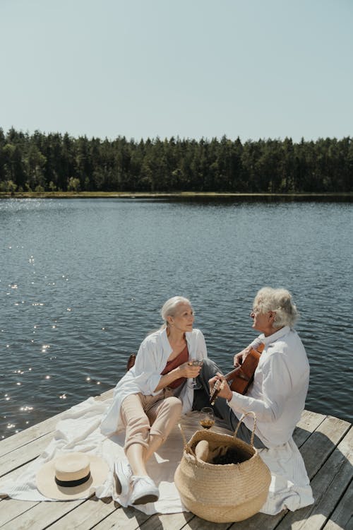 Man and Woman Sitting on White Wooden Dock