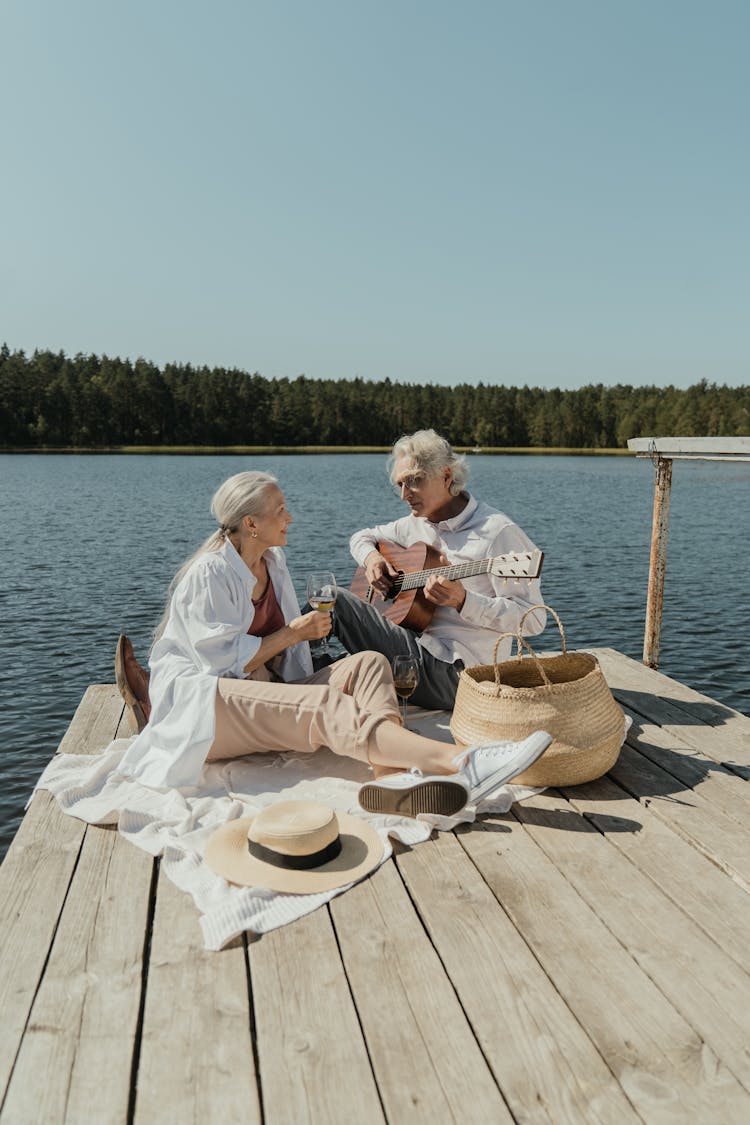 An Elderly Couple Sitting On A Wooden Dock