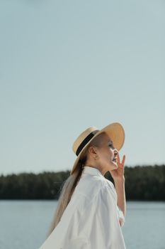 在晴朗的天空下，一位戴着太阳帽的时尚老妇人侧影，正欣赏着湖边宁静的景色