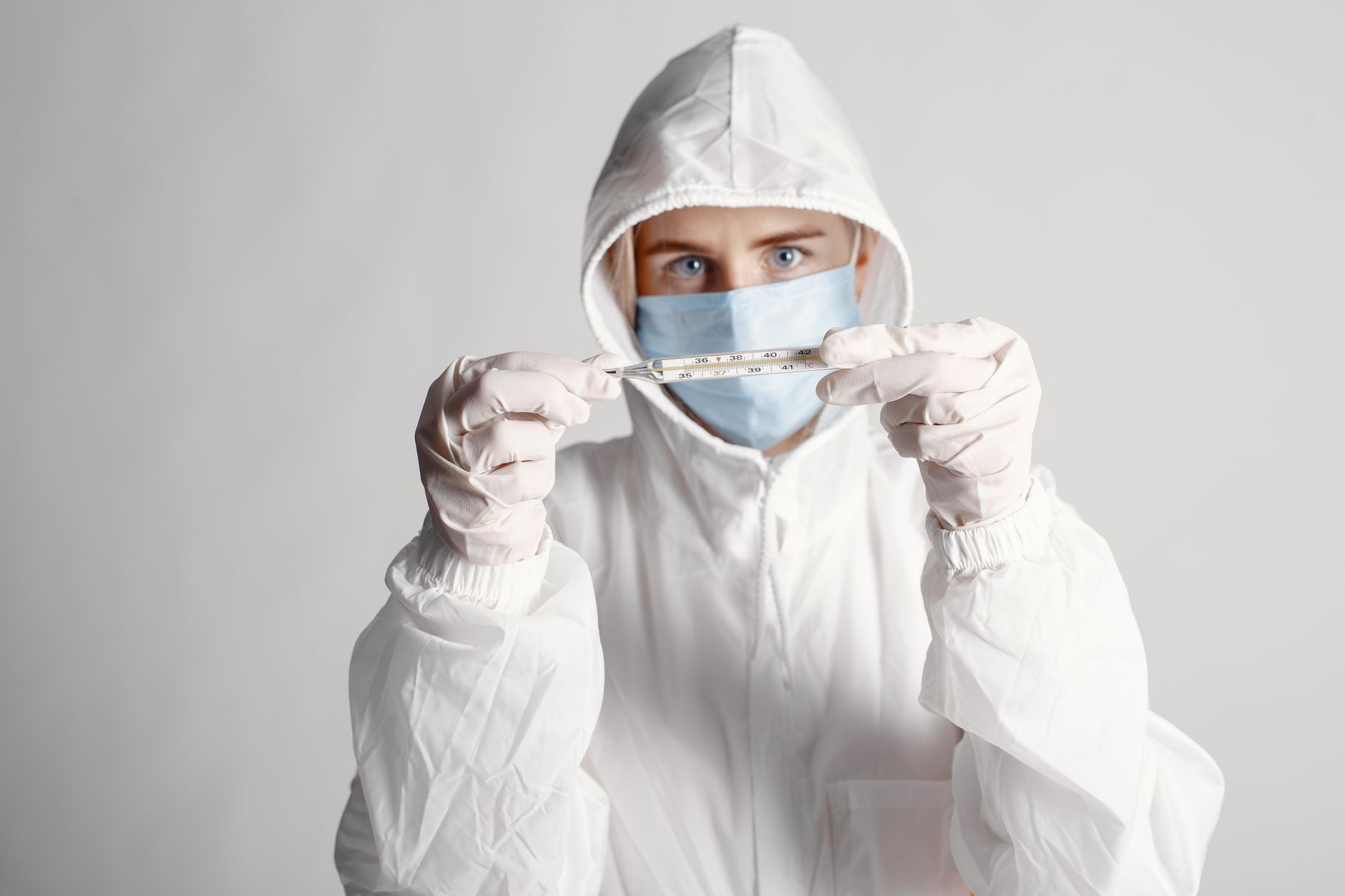 Person in protective suit holding a thermometer during health crisis.