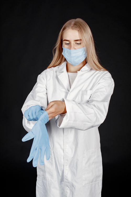 Free A female healthcare worker wearing a mask and gloves, preparing for a medical procedure in a studio setting. Stock Photo