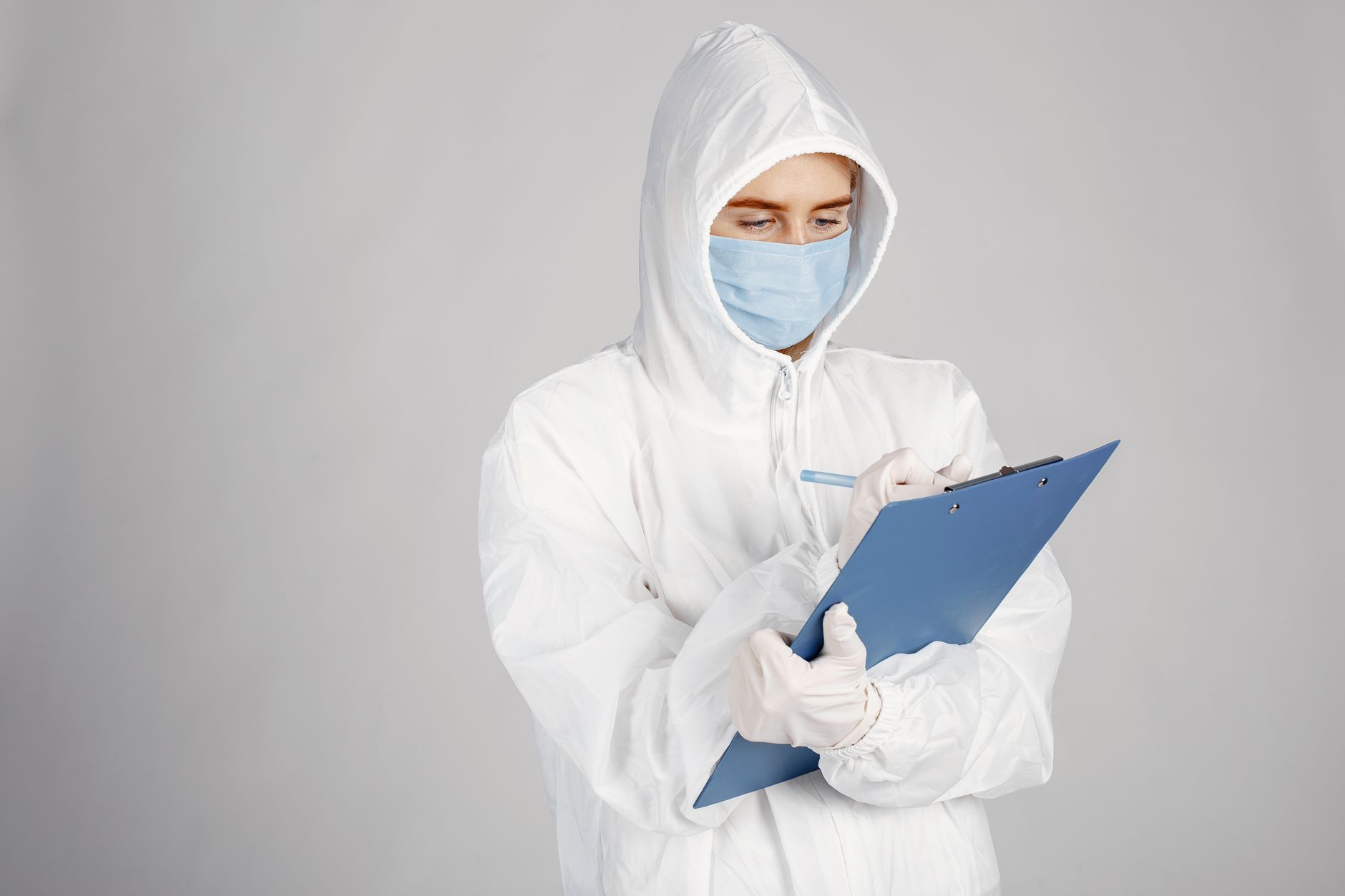 Healthcare professional in PPE suit writing on clipboard in a clinical setting.