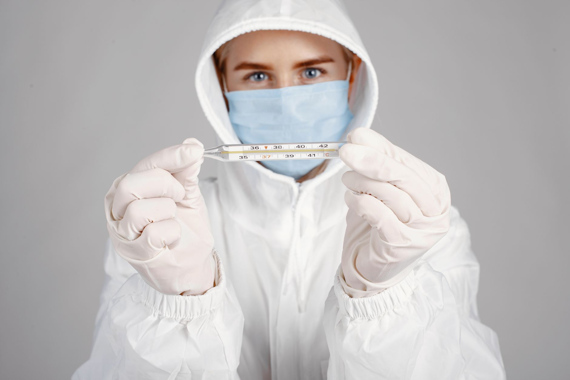 Healthcare professional in PPE holding thermometer for temperature check.