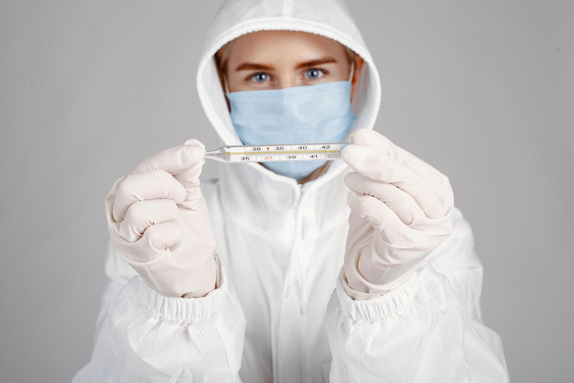 Healthcare professional in PPE holding thermometer for temperature check.