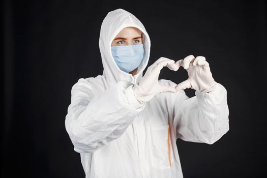 Healthcare professional in full protective gear forming heart symbol with hands, signifying compassion and care.