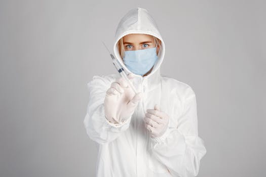 A healthcare professional in protective gear holding a syringe, emphasizing safety and preparedness.