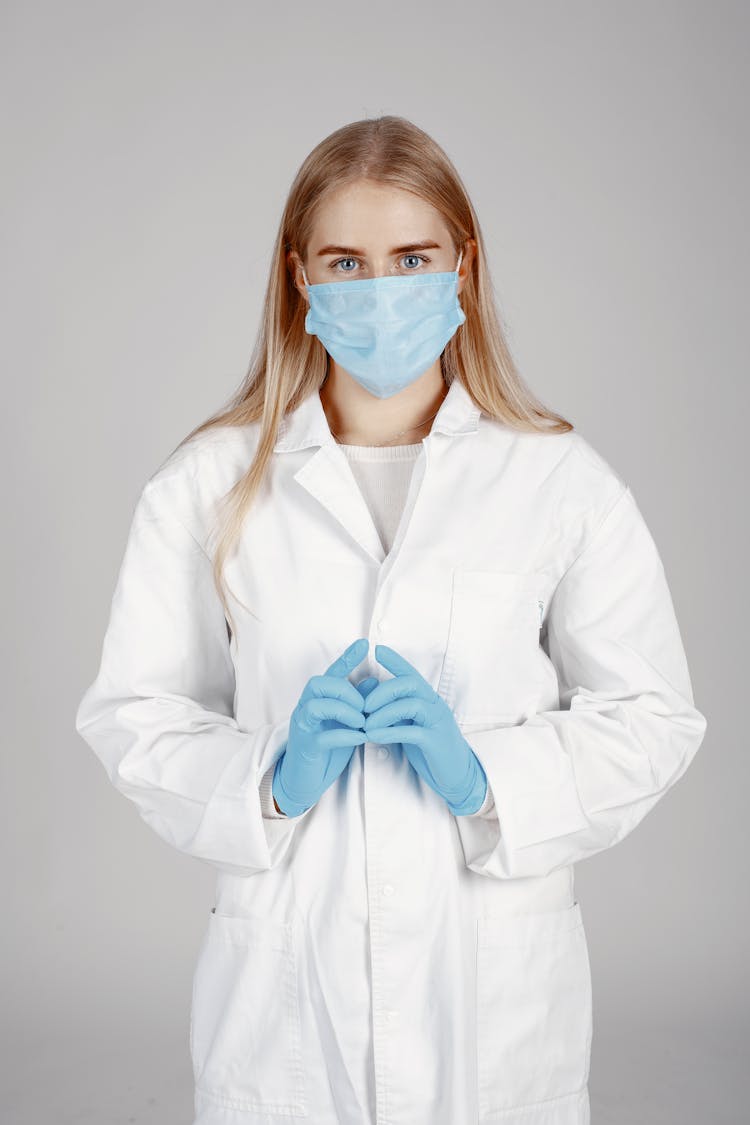 Symmetrical Portrait Of A Blond Woman In White Coat With Blue Gloves And Face Mask